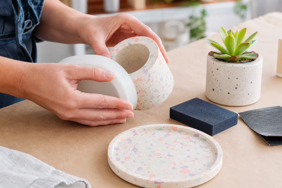 Hands demoulding a pastel terrazzo plant pot beside a matching tray